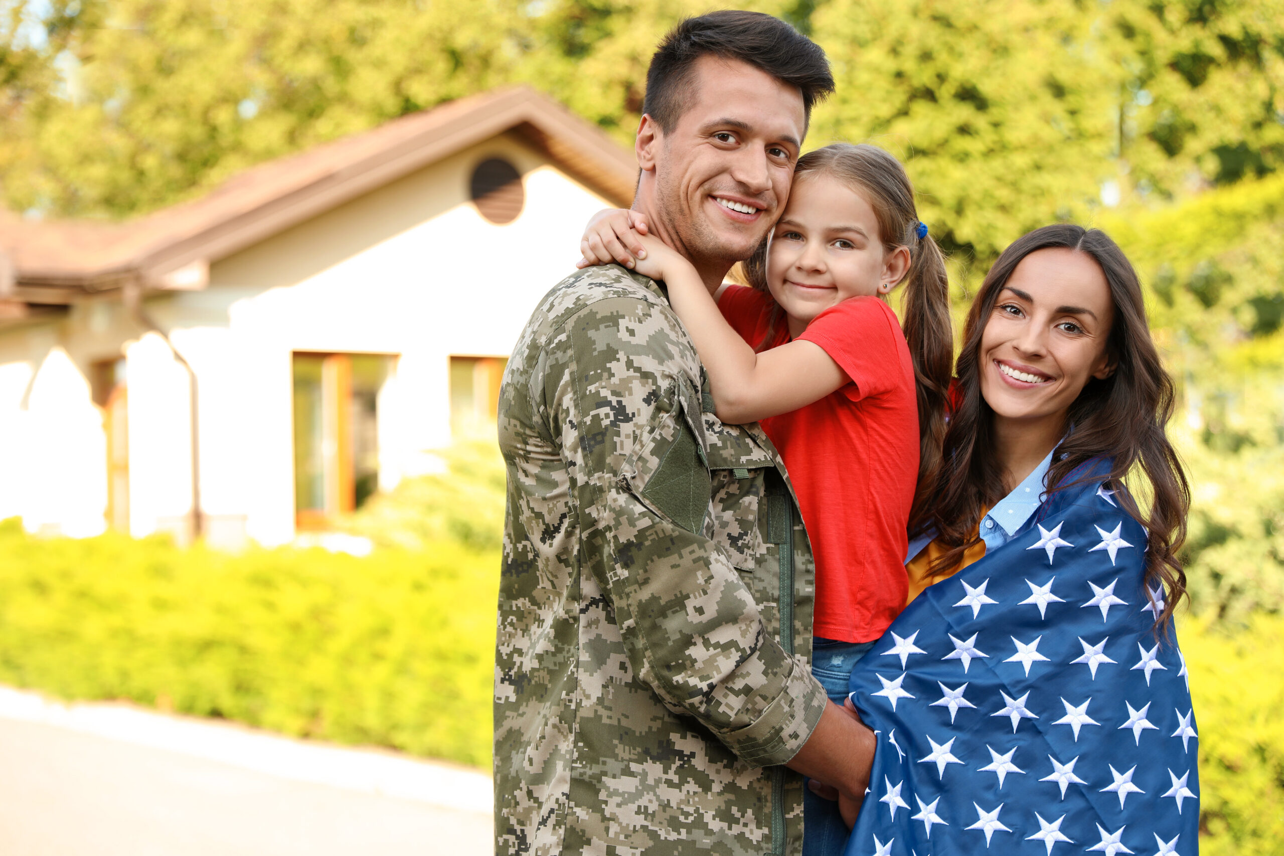 Smiling family holding an American flag outside their suburban home